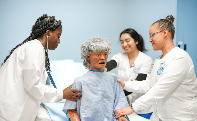 Female nursing student checks pulse of mannekin in lab setting.